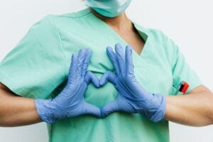 person in gloves making the hearts sign over their chest
