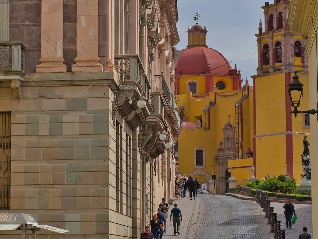 A pillared building in the foreground with a yellow church and red domed roof in the background