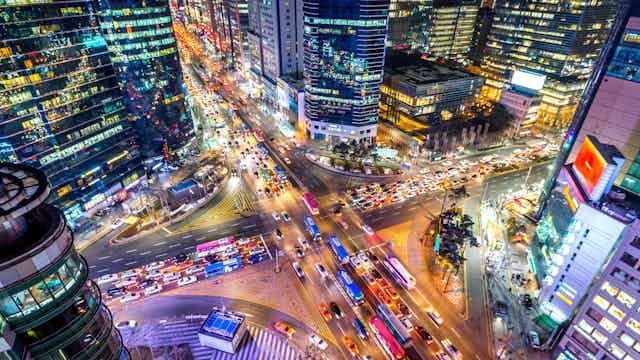 Nighttime aerial view of a busy colourful intersection in Seoul, with vivid colours and a sense of bustling life.