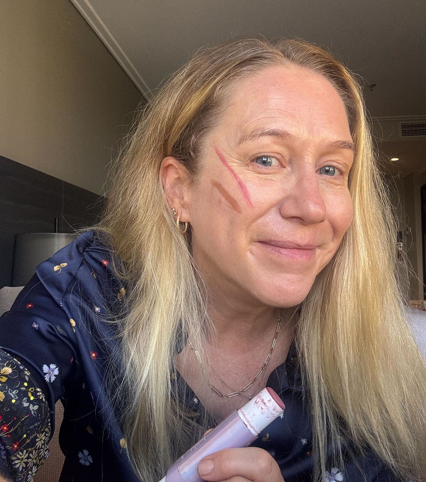 Selfie of Holly holding a blush stick with a line of blush on her cheekbone.