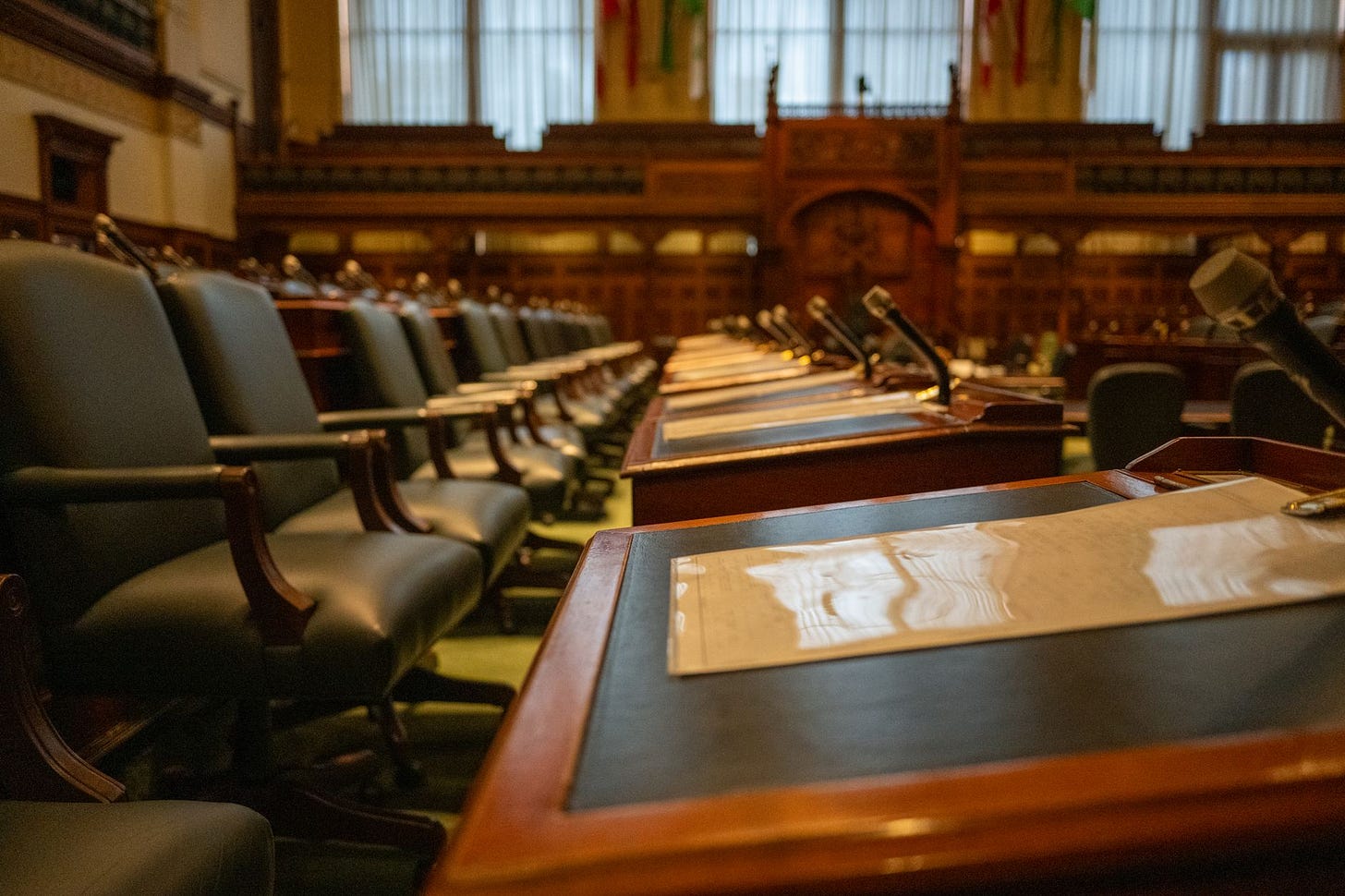 Photo by Héctor Berganza on Pexels A detailed view of an empty legislative chamber with rows of desks and microphones, evoking governance. (stock photo)