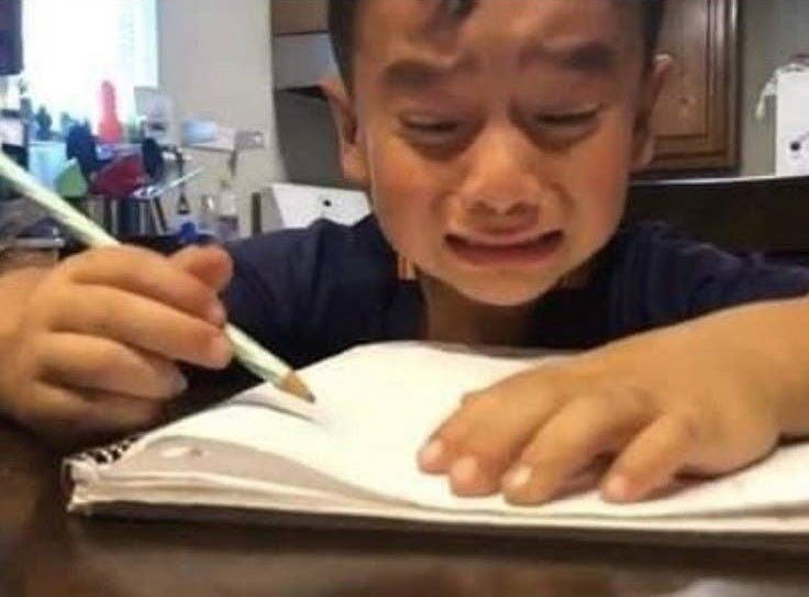 This may contain: a young boy sitting at a table with a pen and paper in front of him