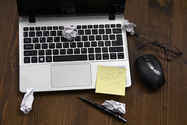 Close-up of a laptop with a yellow sticky note reading "HELP" and crumpled paper around it, symbolizing the need for IT support services in Adelaide.