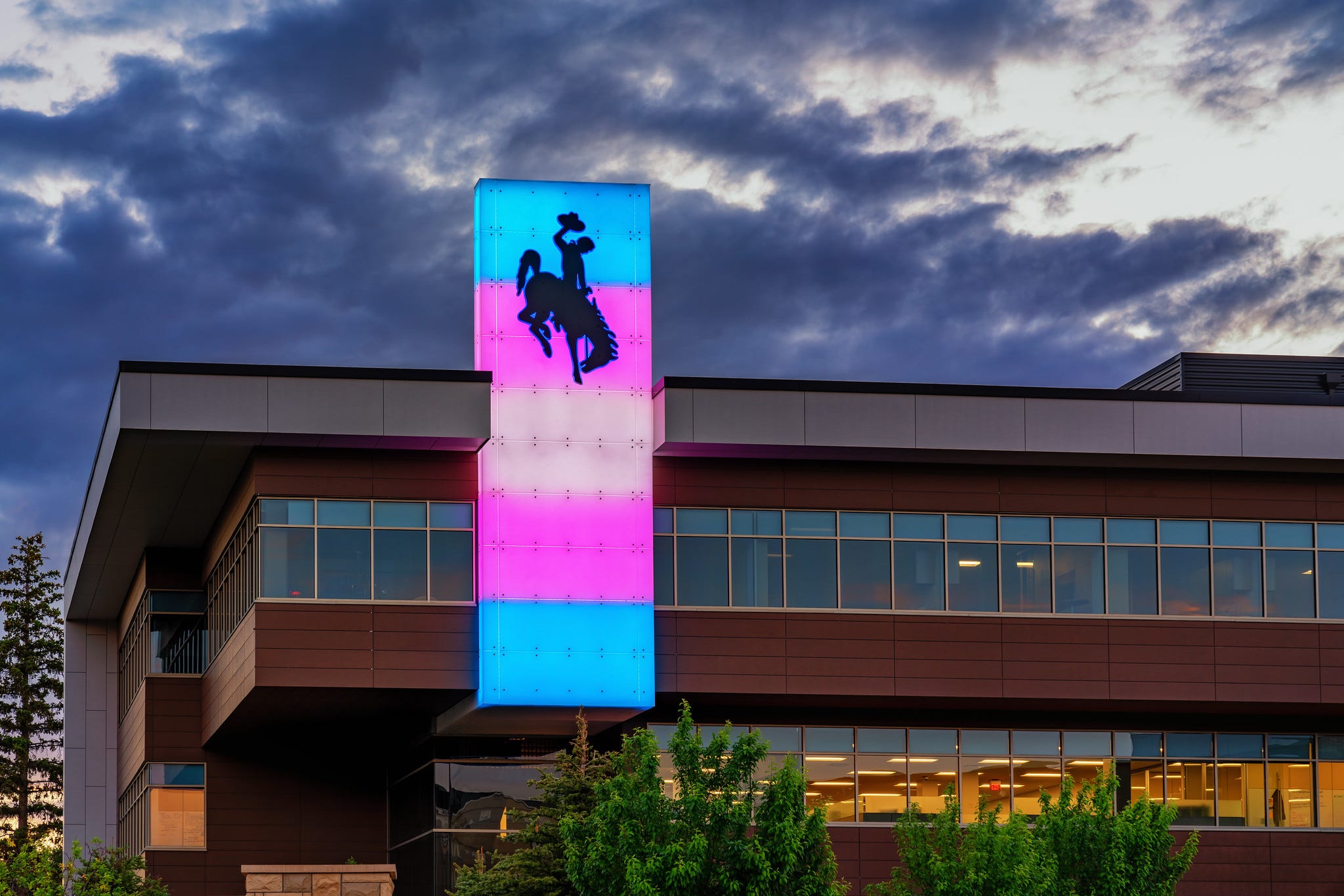 Blue pink and white lights illuminate a steamboat-adorned column on the Rochelle Center. HDR image showing dark cloudy skies in the background. Blue pink and white lights illuminate a steamboat-adorned column on the Rochelle Center. HDR image showing dark cloudy skies in the background.