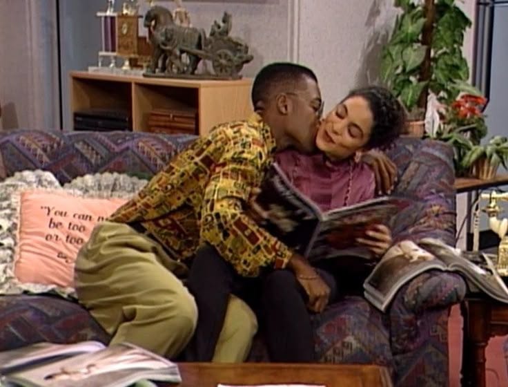 This may contain: a man and woman kissing on the couch in front of a coffee table with books