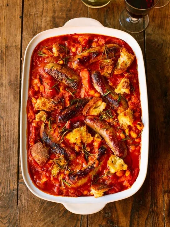 Sausage traybake in a baking dish with tomatoes, creamy white beans and garlic