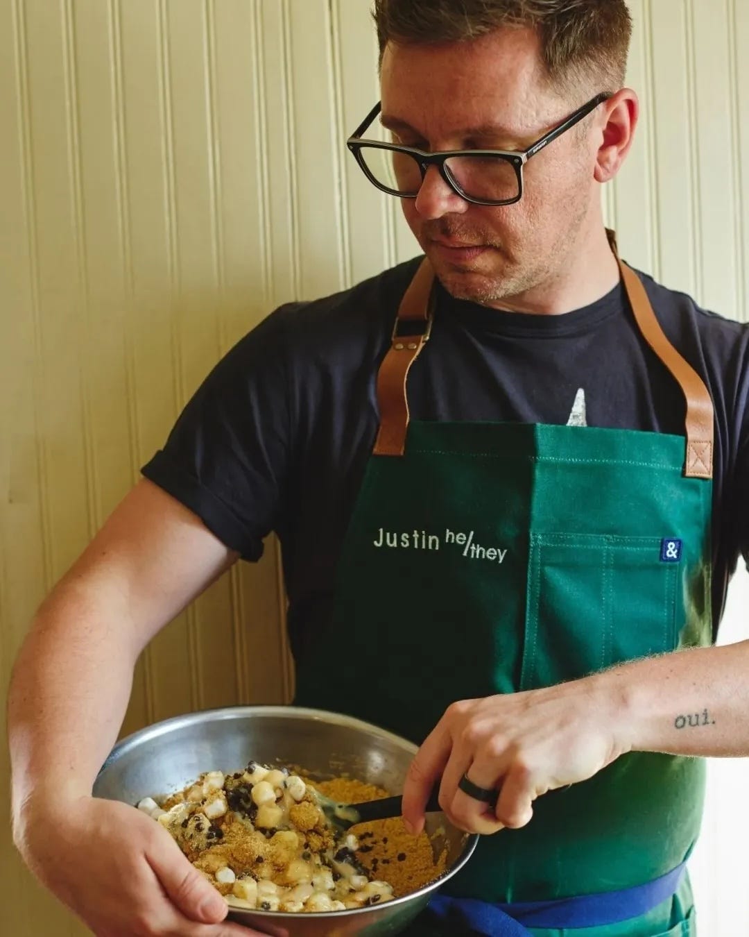 Justin wearing his apron and stirring a cookie mix in a silver bowl Justin wearing his apron and stirring a cookie mix in a silver bowl