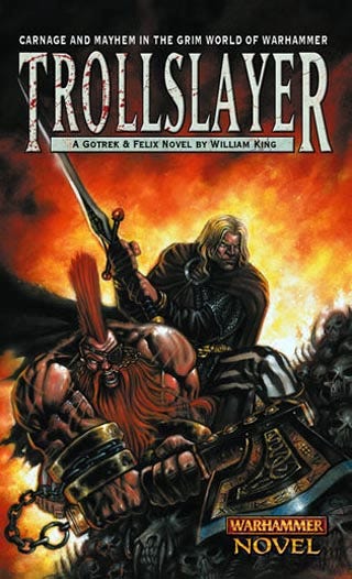 The cover of Trollslayer's first edition. Gotrek and Felix stand atop a pile of bones - human and otherwise, the background in flames. The text reads: "Carnage and mayhem in the grim world of Warhammer. Trollslayer: A Gotrek & Felix novel by William King.”