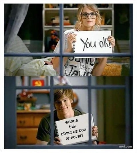 Two stills from a music video of neighbours holding up signs in facing windows. Her sign: "You ok?" His sign: "wanna talk about carbon removal?"