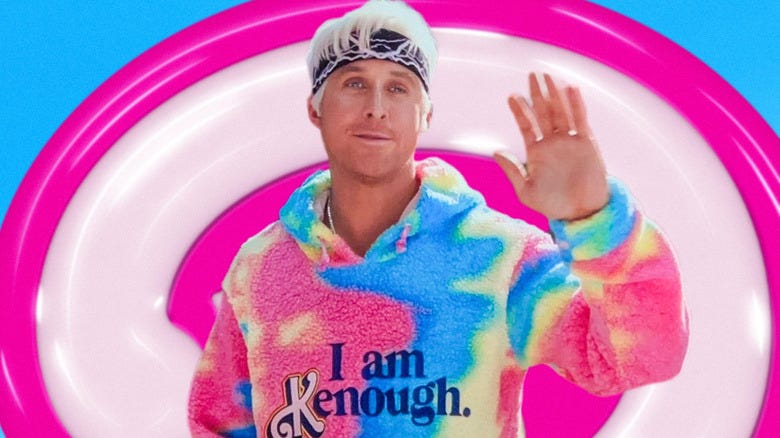 a man with platinum hair wearing a fuzzy, tie-dye colored sweatshirt that says, "I am Kenough"