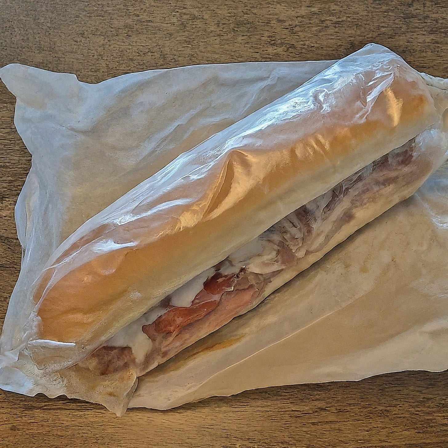 Submarine sandwich with meat, cheese, and veggies, wrapped in plastic like Laura Palmer. AI generated image.