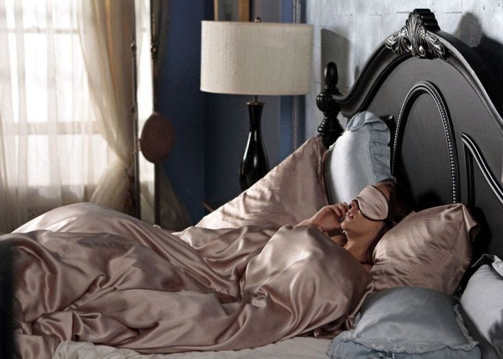 This may contain: a woman laying on top of a bed in a bedroom next to a lamp and window
