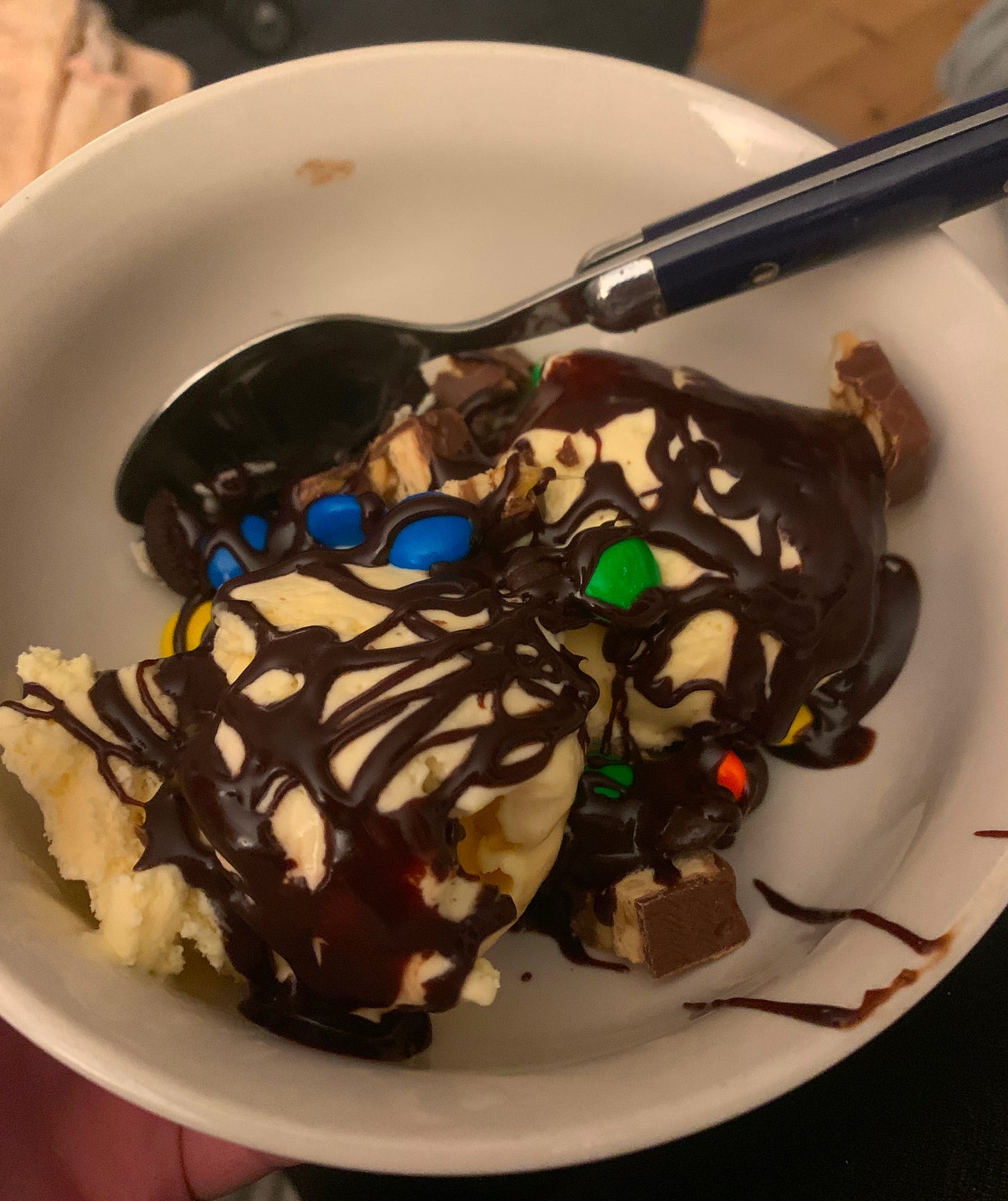 vanilla ice cream with chocolate sauce and candy in a white bowl
