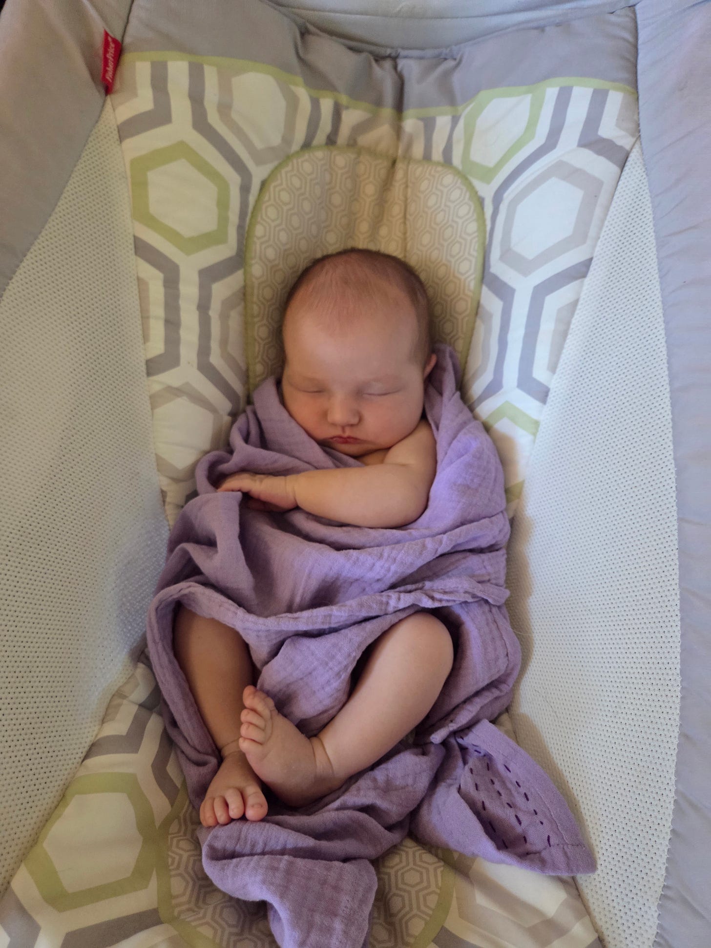 A sleeping baby in a rocker, wrapped in a purple blanket with her fingers and toes hanging out, because of all her wriggling.