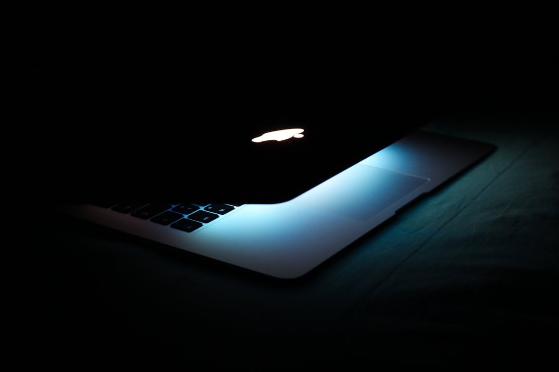 Free A partially closed laptop with a glowing logo and illuminated keys in a dark setting. Stock Photo
