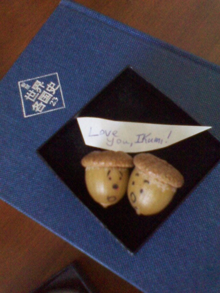 ふたつのドングリの写真。ドングリには顔が書いてある。小さな紙切れにLove You, Ikumiとメッセージが書いてある。