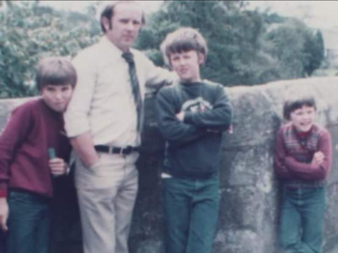 A blurry photo of a man and 3 boys standing by a wall 