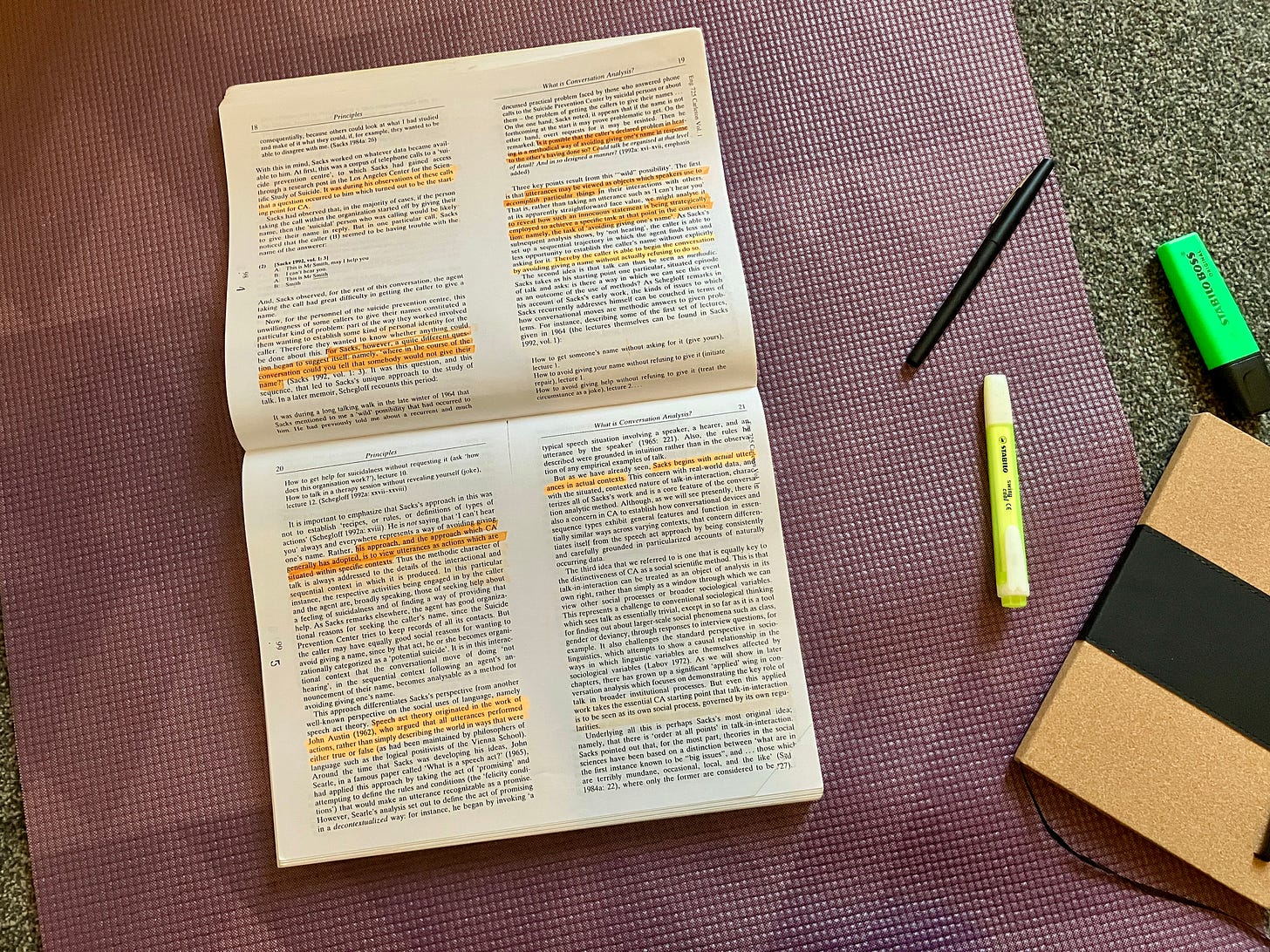 An academic workbook is open on a purple yoga mat. Pens and highlighters are strewn about.