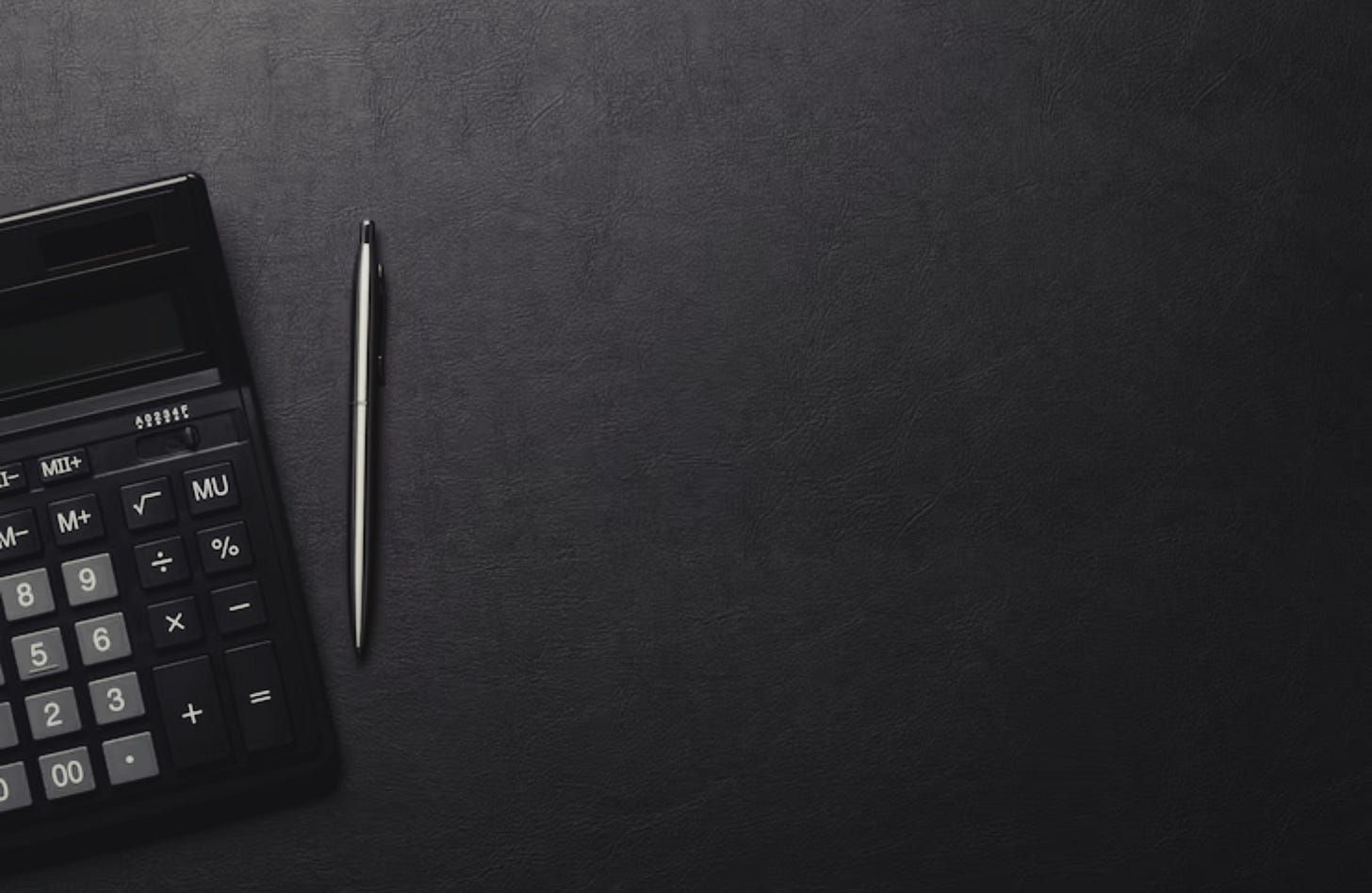 A dark image of a calculator and pen on a black table.