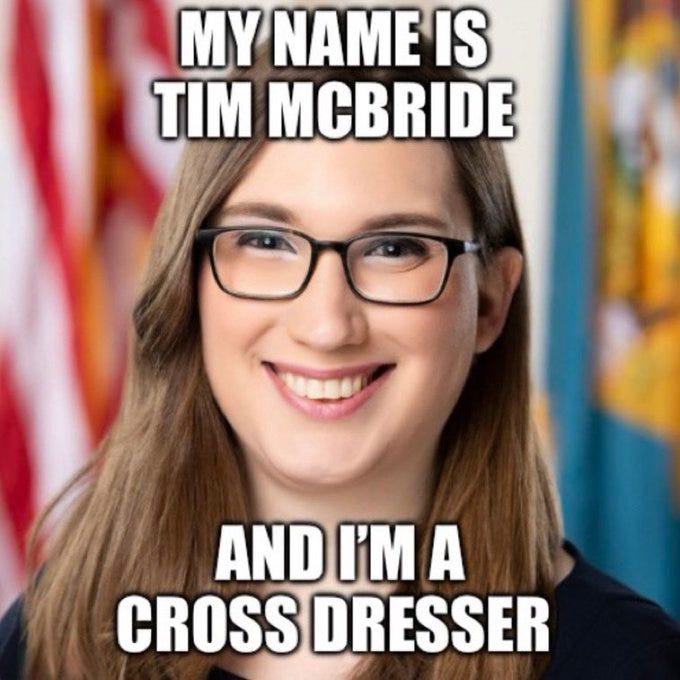 A photo of Tim McBride, a person with long brown hair and glasses, smiling. The background includes an American flag and a colorful banner. Text overlay reads "MY NAME IS TIM MCBRIDE AND I\'M A CROSS DRESSER."