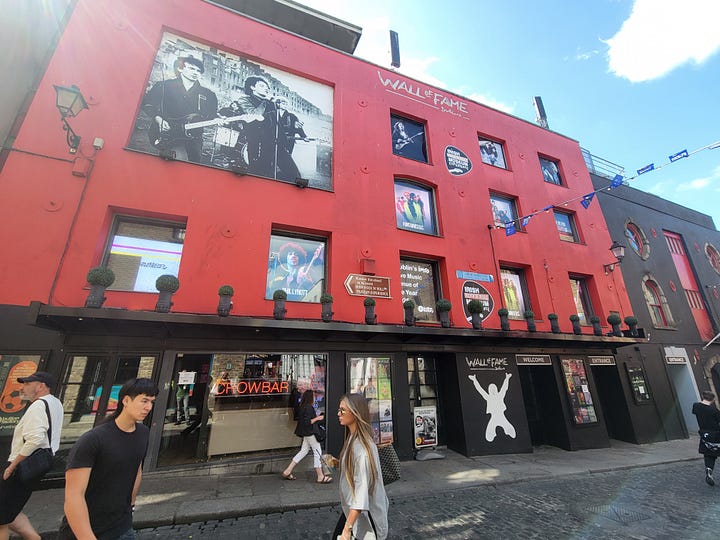 Five photos from the Irish Rock and Roll Museum and Temple Bar district. First, my daughter next to a photo of the band, U2. A display of three vintage guitars. The museum's Wall of Fame exterior and a streetscape in Temple Bar.
