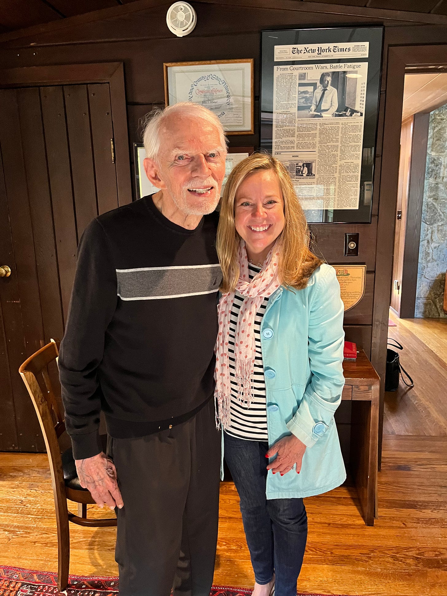 An elderly man and a middle aged woman stand in a wood paneled office in front of framed news clippings and photographs. The man is author John Martel, and the woman is memoir-writing coach and developmental editor Christine Wolf An elderly man and a middle aged woman stand in a wood paneled office in front of framed news clippings and photographs. The man is author John Martel, and the woman is memoir-writing coach and developmental editor Christine Wolf