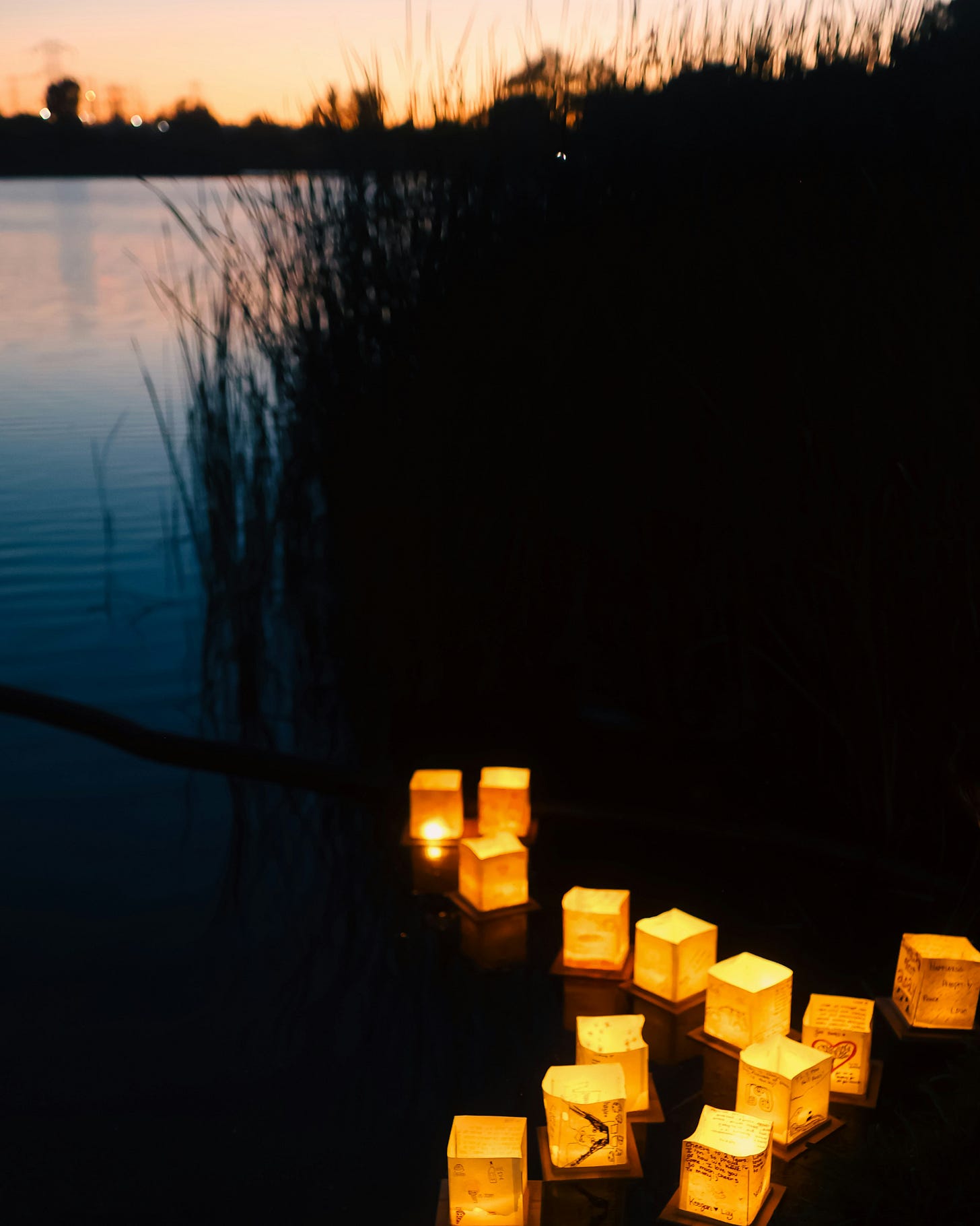 Paper lanterns glowing on still water at dusk, a small cluster of lights gathering in the dark.