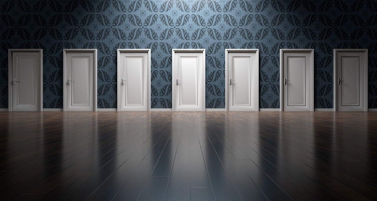 Seven white doors in a large room with blue patterned wallpaper and polished wood floors