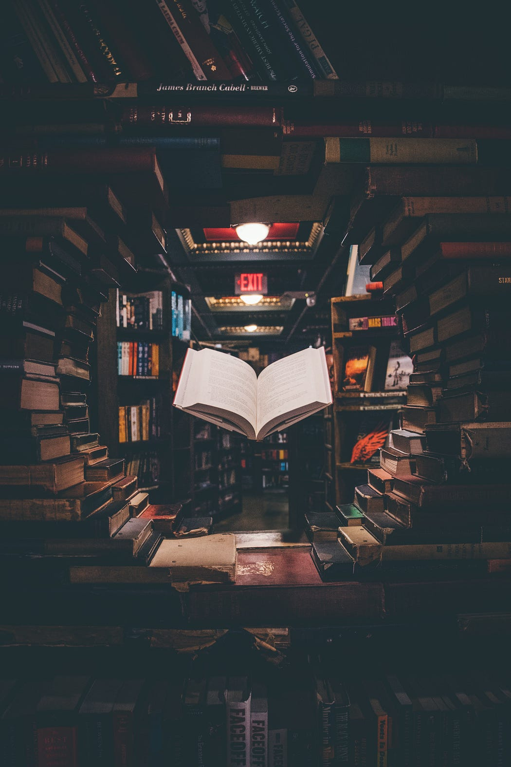 Artistically stacked tunnel of used books with one book that appears to be floating open in the center of the tunnel
