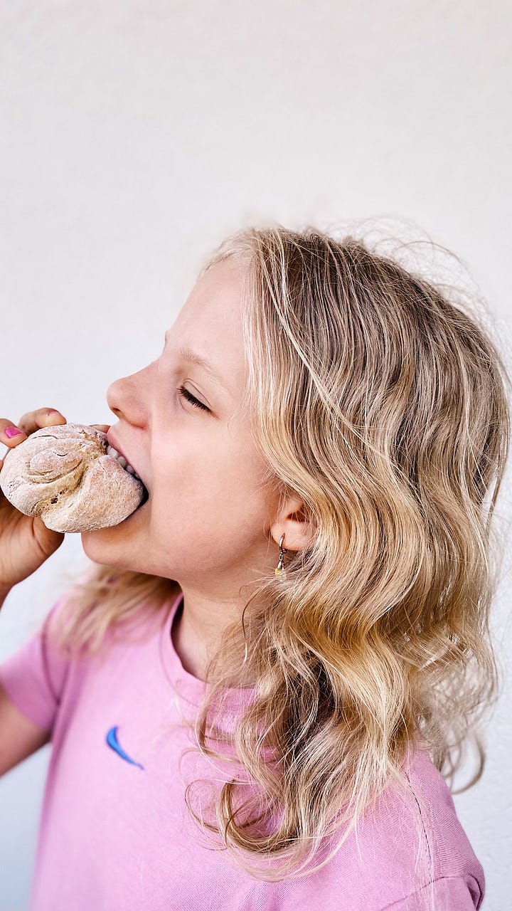 A bun on a marble surface and a blond curly girl biting a bun, smiling