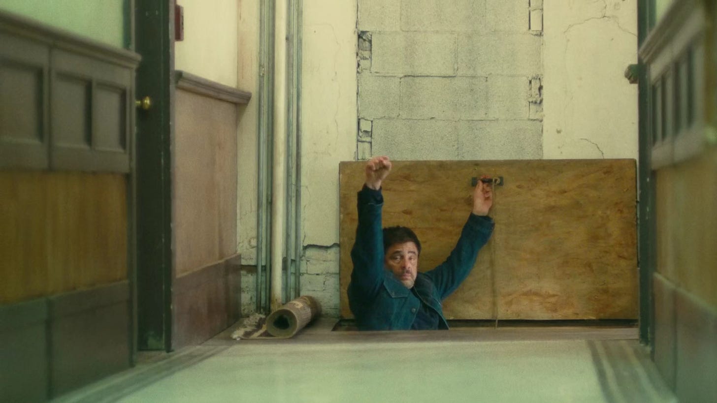 Sensei halfway down a hidden trapdoor holds his fist up in a salute