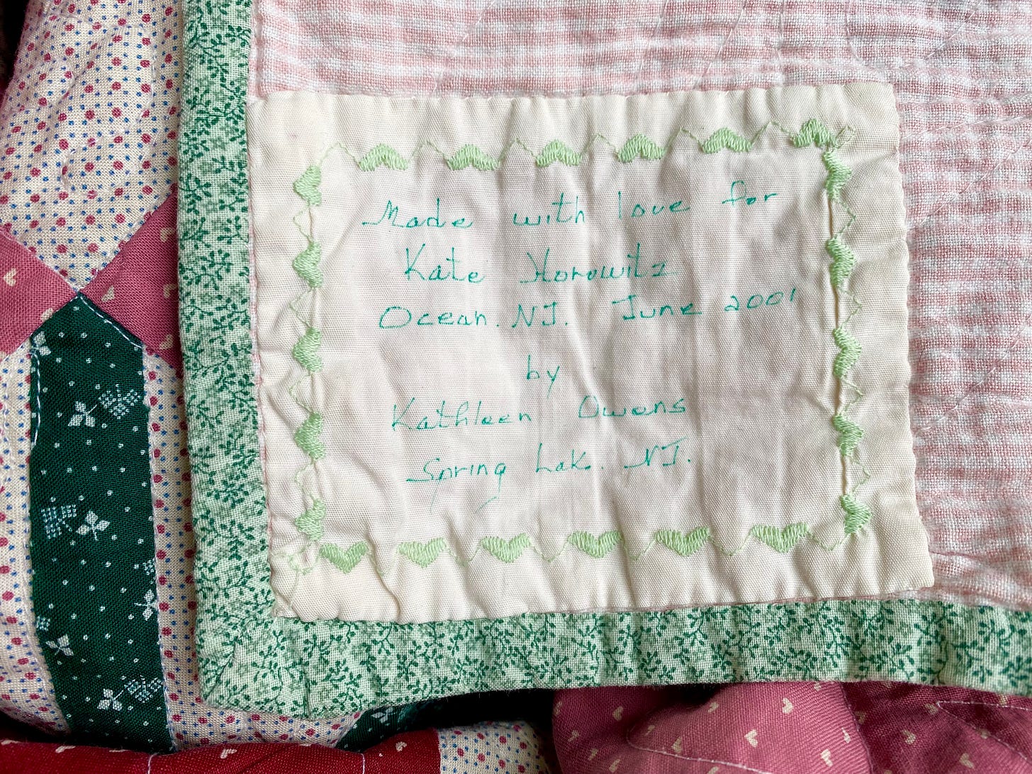 Closeup of a patchwork quilt. The handwritten label says "Made with love. Kate Horowitz, Ocean, NJ. June 2001. by Kathleen Owens, Spring Lake, NJ.