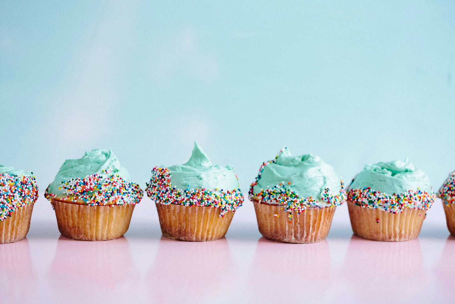 a line of cupcakes with frosting and colored sprinkles sitting on a pink table