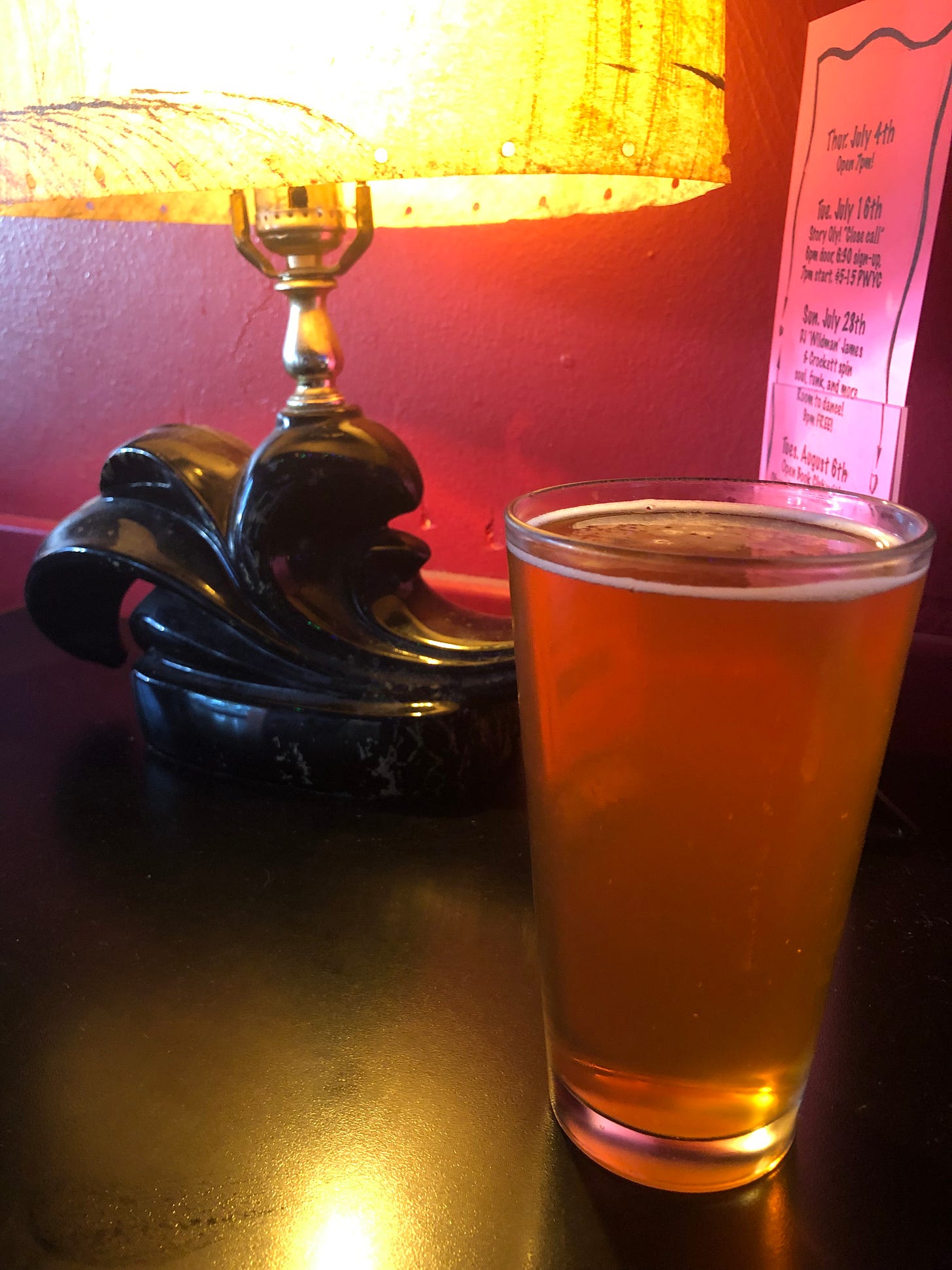 A beer, Boneyard RPM IPA, on a black laminate table with a mid-century lamp behind it, against a red wall. A beer, Boneyard RPM IPA, on a black laminate table with a mid-century lamp behind it, against a red wall.