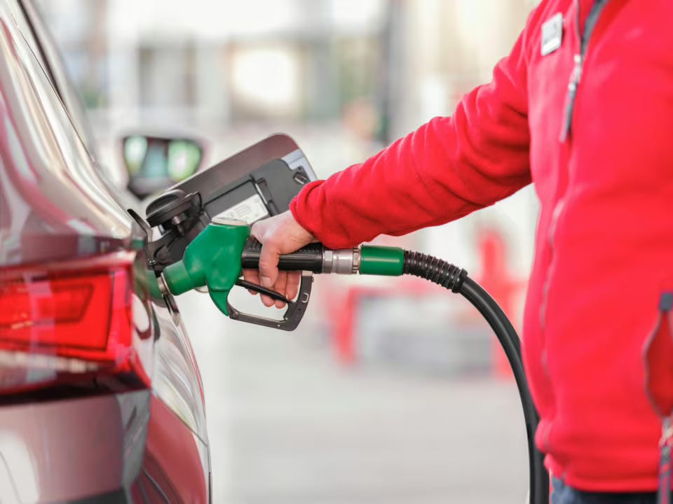 A man wearing a red jumper fills up a red car with petrol.
