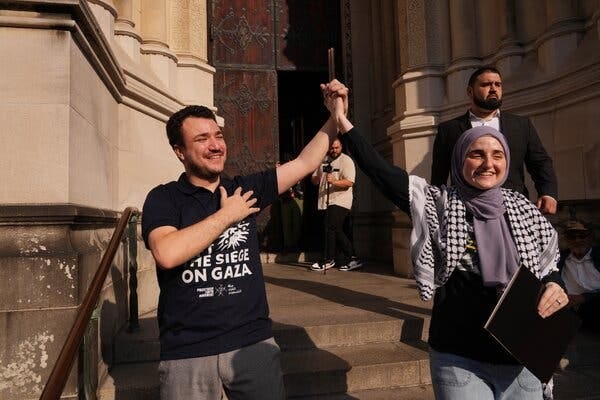 A man wearing a black shirt with the words “The Siege on Gaza” joins hands with a woman wearing a head scarf and kaffiyeh.