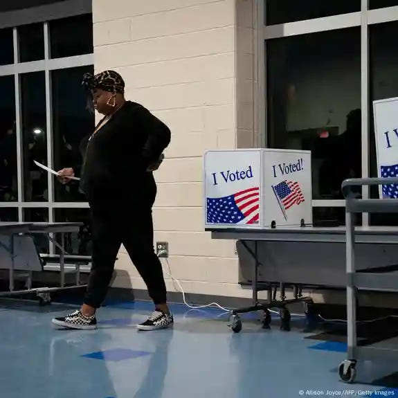 A Black woman walks away from polling stations emblazened with the US flag and the "I voted" slogan after voting A Black woman walks away from polling stations emblazened with the US flag and the "I voted" slogan after voting