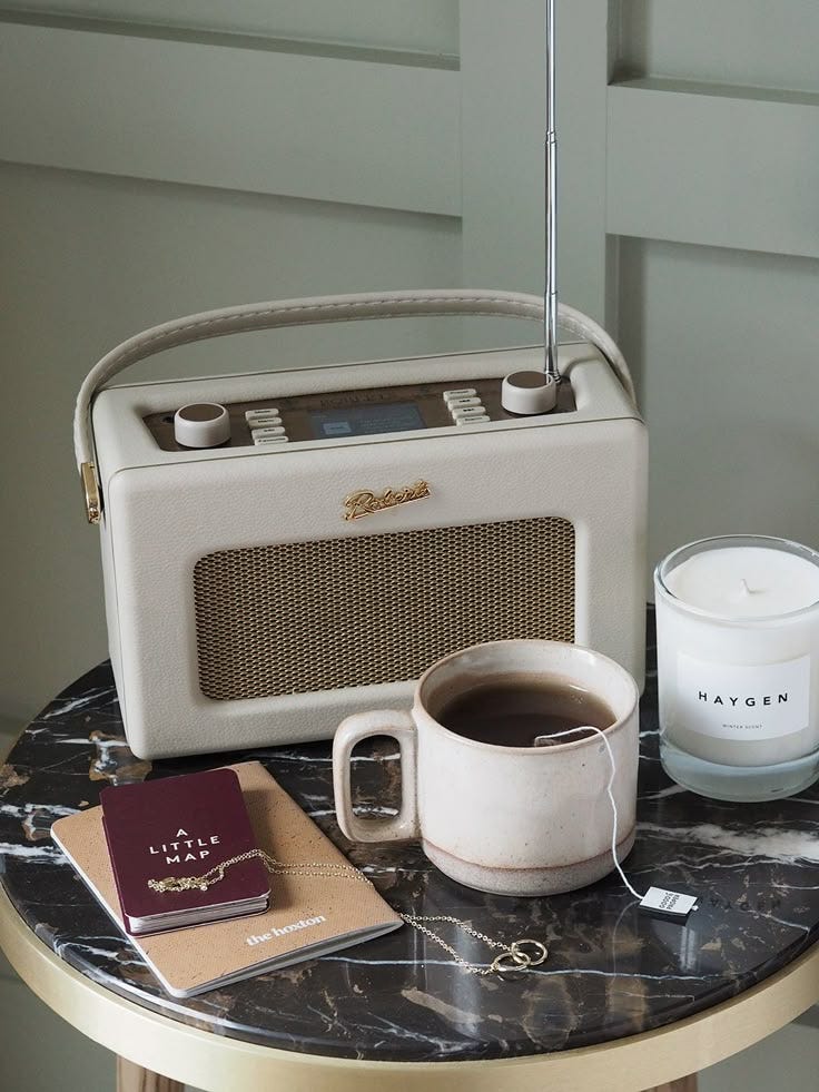 This may contain: a table topped with a radio, cup of coffee and a candle on top of it