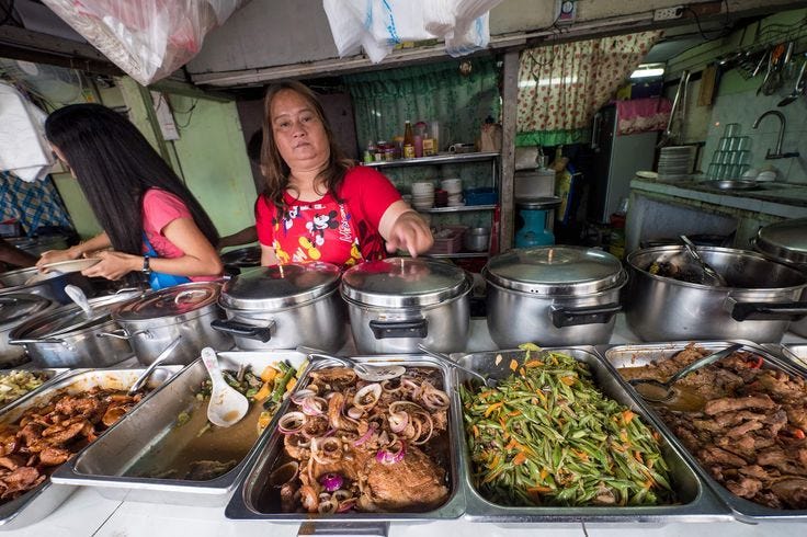 This may contain: a woman standing behind a counter filled with lots of food