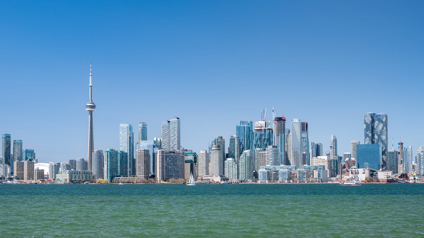 The downtown Toronto skyline seen across the water from the Toronto Islands on a clear day, with the CN Tower at left and a single sailboat on the green-blue lake in the foreground. The downtown Toronto skyline seen across the water from the Toronto Islands on a clear day, with the CN Tower at left and a single sailboat on the green-blue lake in the foreground.