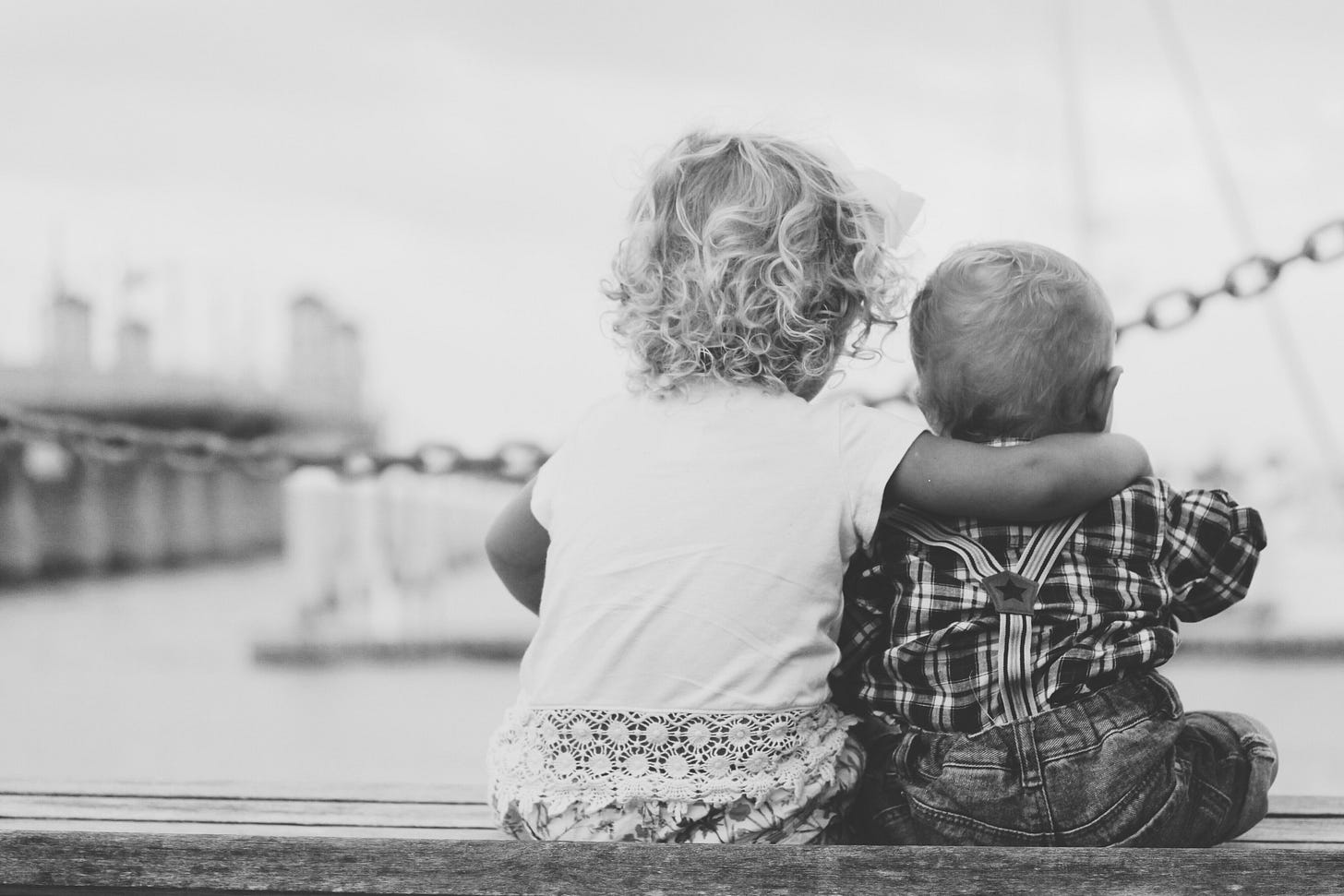 A toddler and a baby sit side by side, the toddler has their arm around the baby’s shoulder (photo by Joshua Clay on Unsplash). A toddler and a baby sit side by side, the toddler has their arm around the baby’s shoulder (photo by Joshua Clay on Unsplash).
