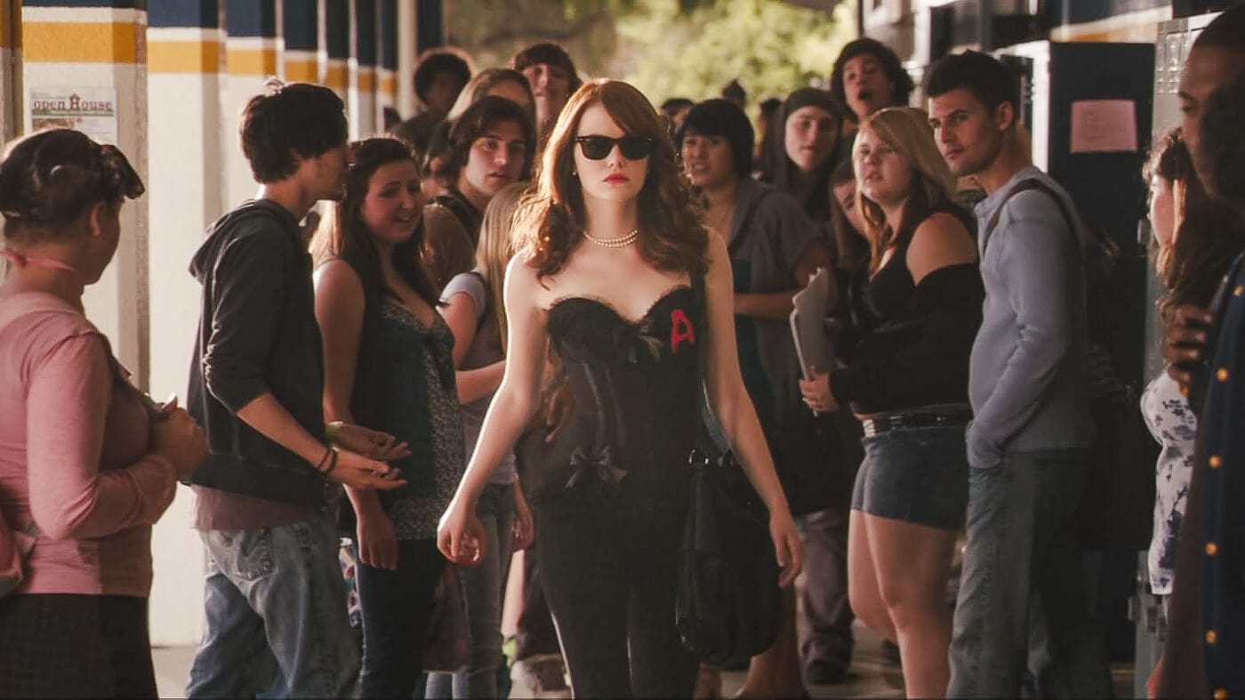 Emma Stone struts confidently past the lockers of her high school wearing dark shades and a black halter top emblazoned with a red A for Adultery on her chest, while her fellow classmates gawk in disbelief watching her pass.