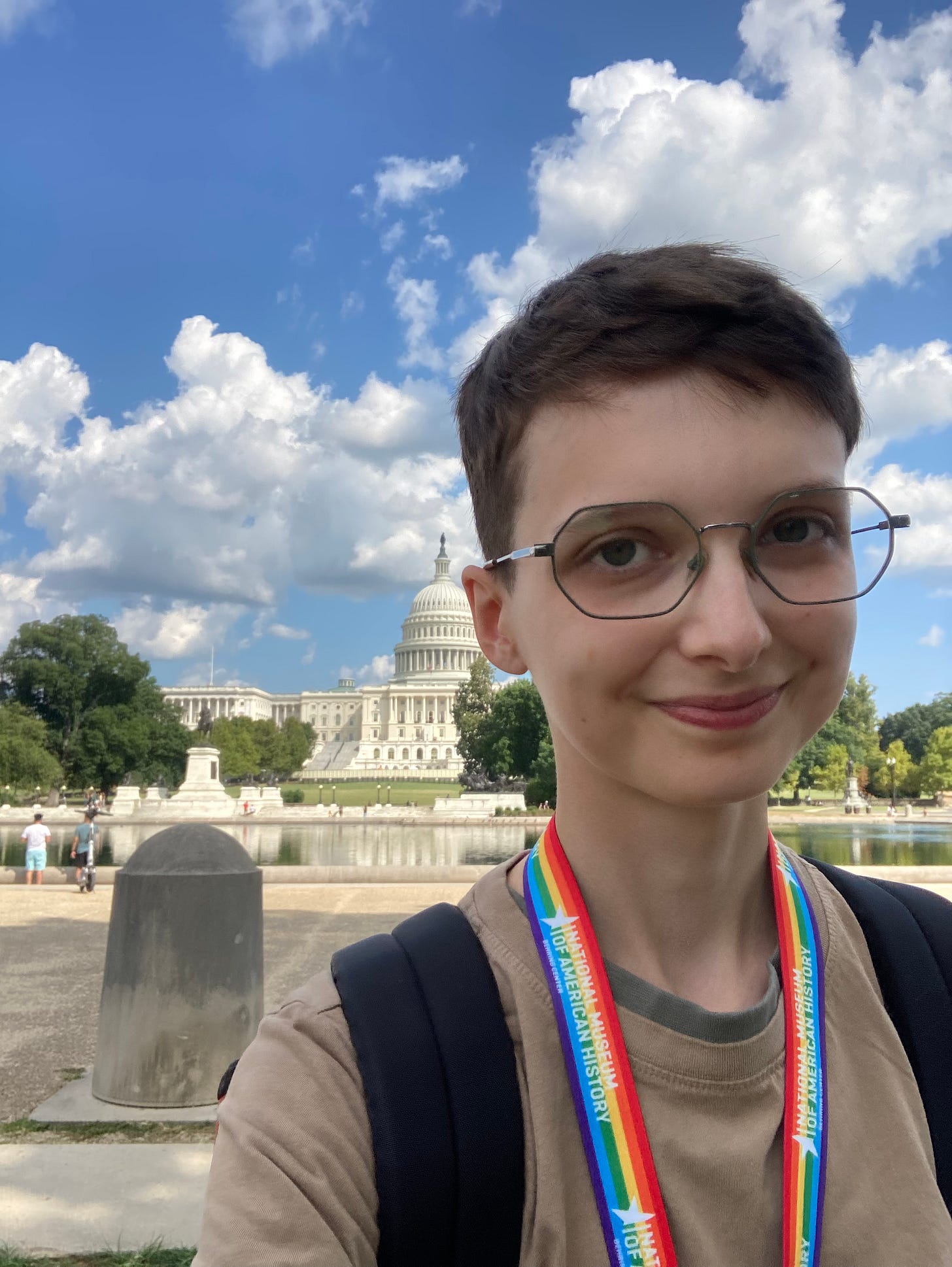 Selfie of Beck wearing a rainbow Smithsonian lanyard, with the Capitol building in the background set against a very blue sky