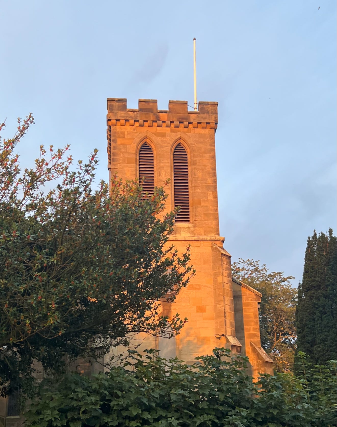 A village church tower in evening sunlight.
