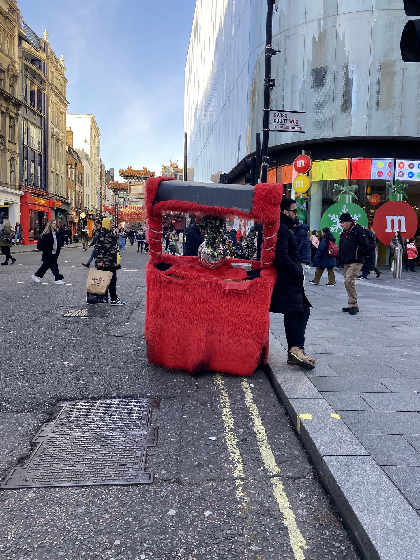 A red fluffy tuk tuk, with a disco ball attached at the back, parked up outside M&M world
