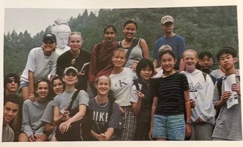 A group of international school students posing together outdoors during a school trip with mountains visible in the background