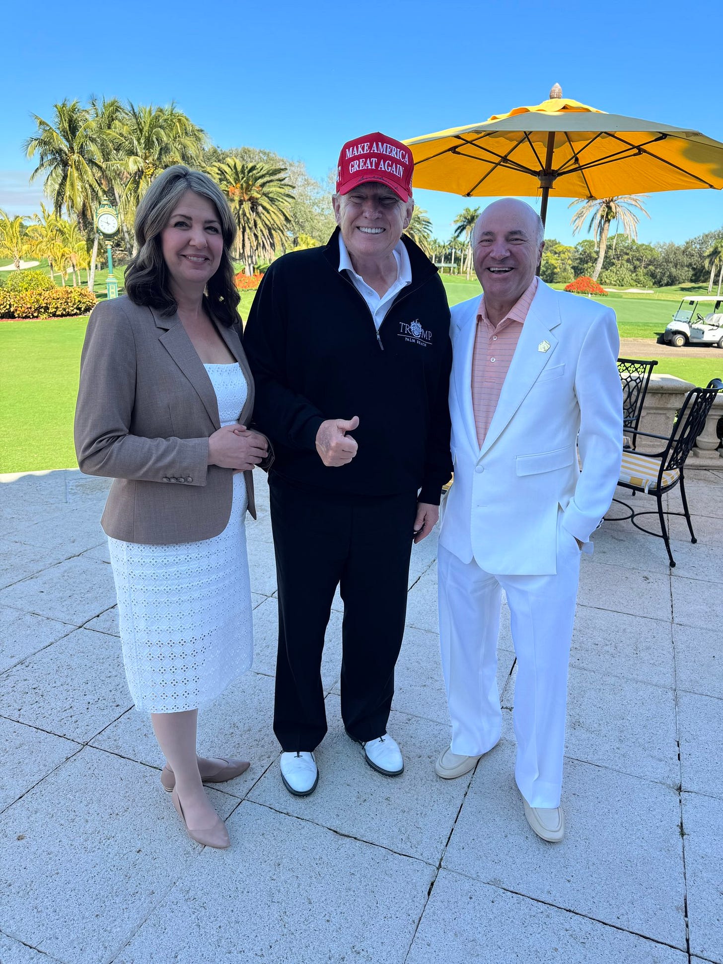 Alberta Premier Danielle Smith posing at a golf course with palm trees in the background beside Donald Trump and Kevin O'Leary at Mar-a-Lago, January 2025