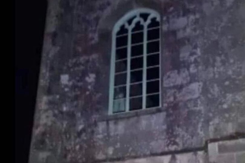 screenshot of church at night centred on an old window which a white shape in the bottom left