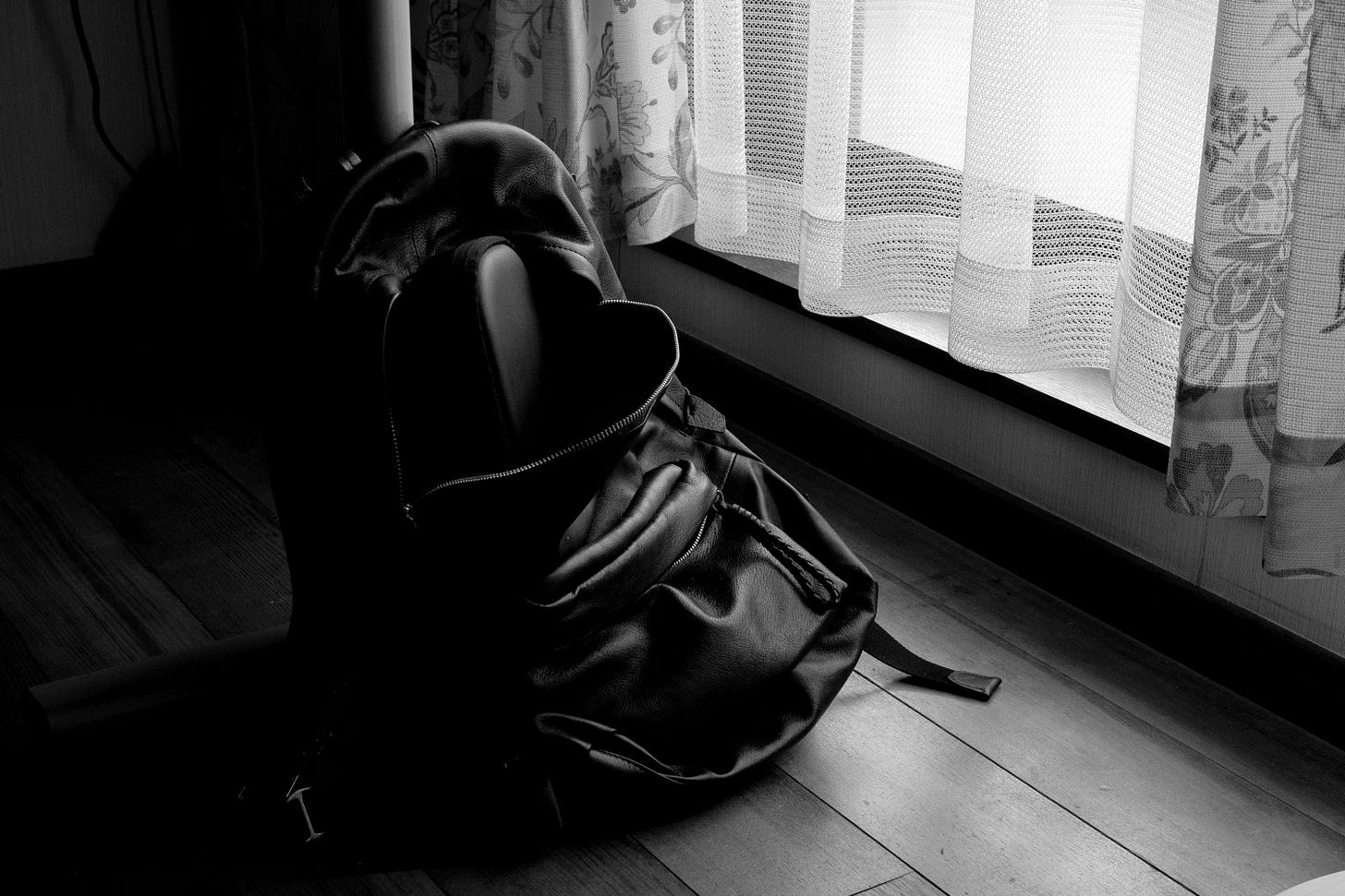 a black backpack sitting on the floor in front of a window a black backpack sitting on the floor in front of a window