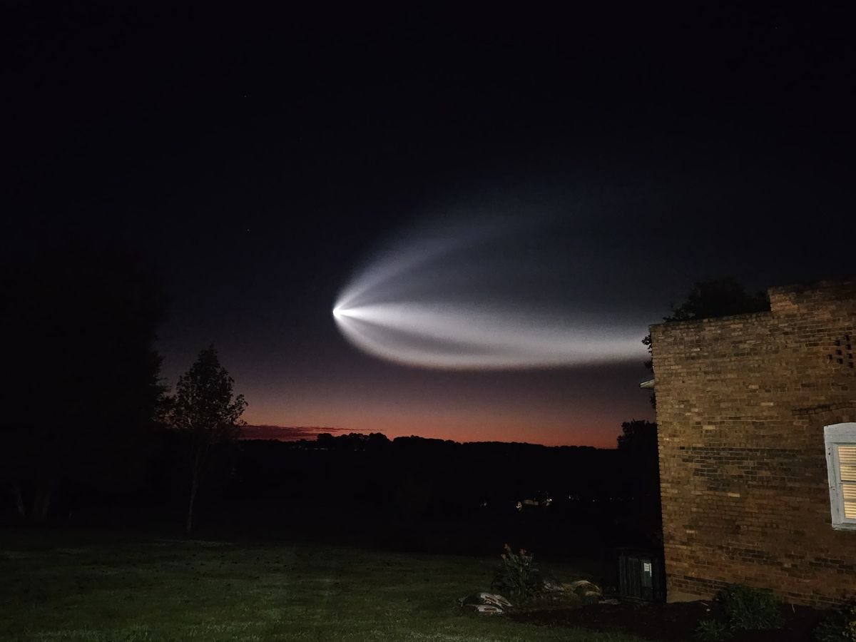 a white streak illuminated in the sky flies over a dark landscape and a brick house. a white streak illuminated in the sky flies over a dark landscape and a brick house.